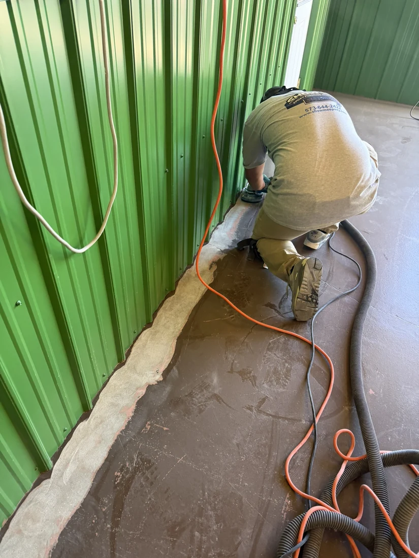 Show Me Epoxy installer edge grinding along a wall base with dust extraction in Belle Missouri